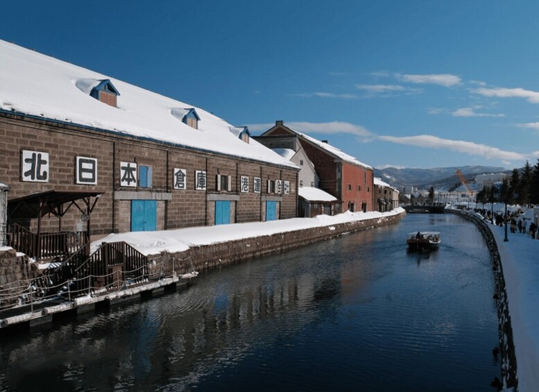 A snow-covered canal with buildings, a boat, and mountains in the background. 2