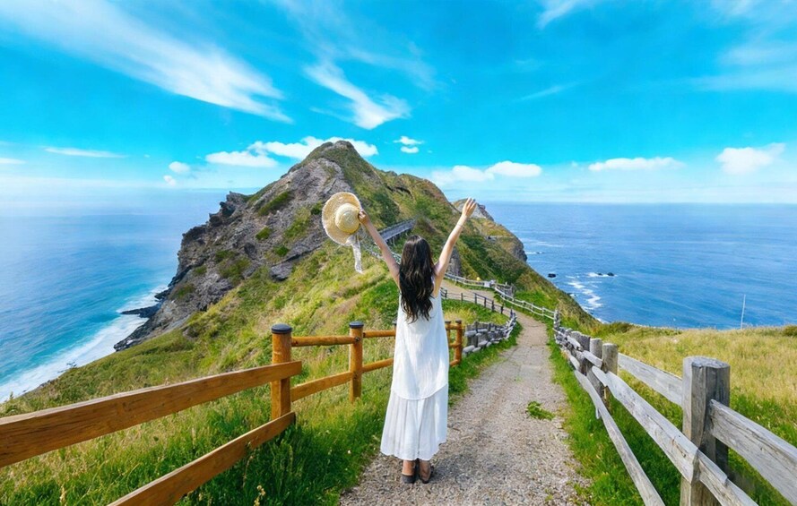 A woman on a coastal trail with a mountain in the background. 1