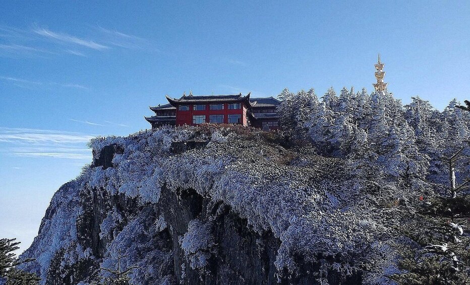 A traditional red building with ornate architecture on a snow-covered cliff. 1