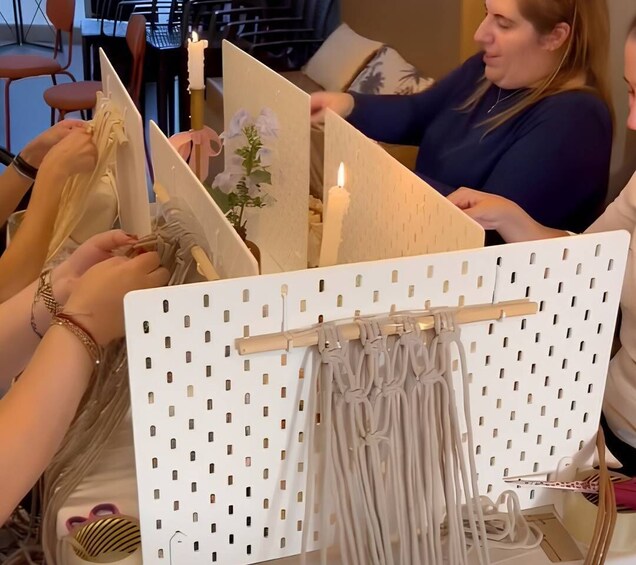 A person sewing on a white board with a pegboard design, surrounded by other individuals engaged in similar activities. 2