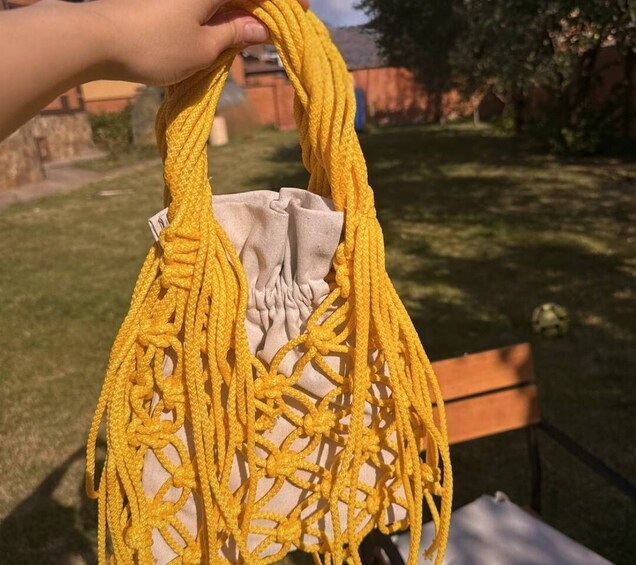 A yellow macrame bag with a beige interior, held by a hand. 3