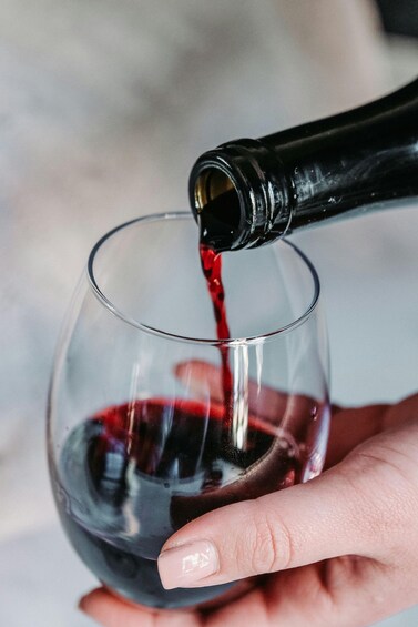 A hand holding a wine glass with red wine being poured into it. 2