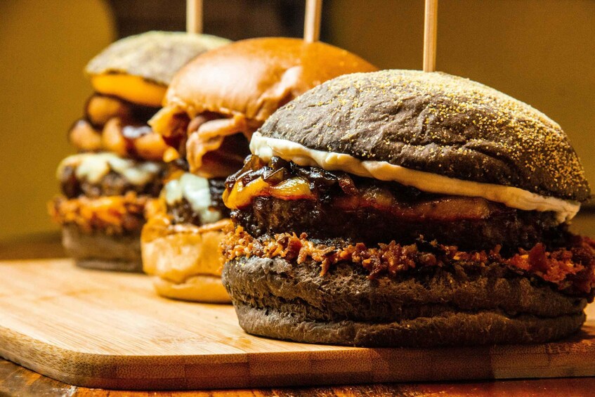 A row of burgers with various toppings on a wooden board. 5