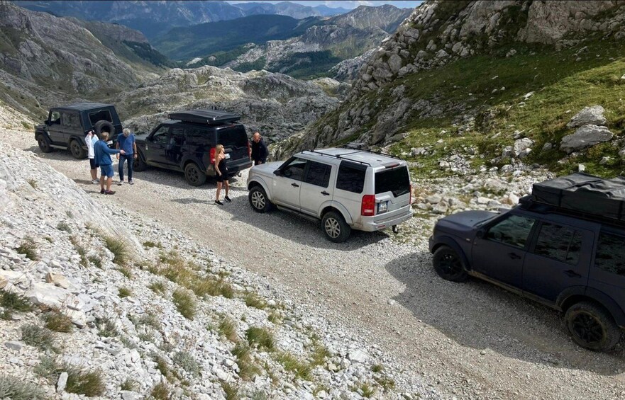 A group of people and vehicles on a gravel road in a mountainous area. 2