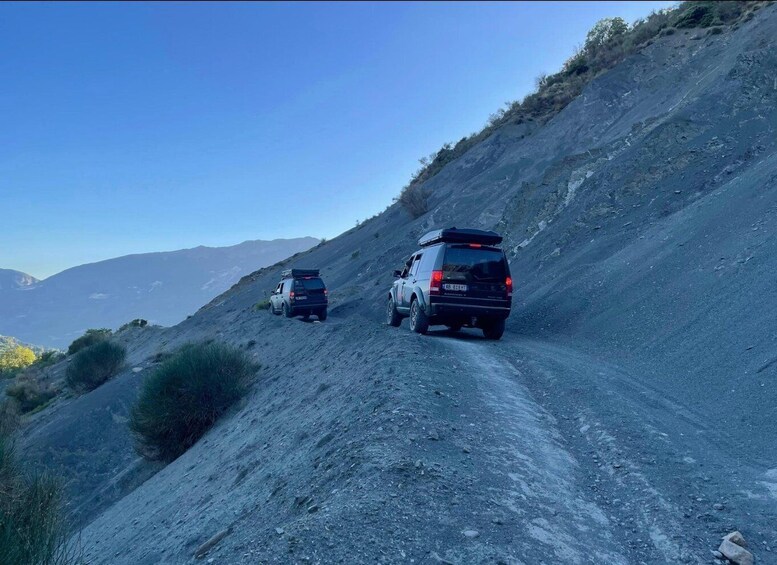 Two vehicles on a steep, rocky road with a clear sky. 3