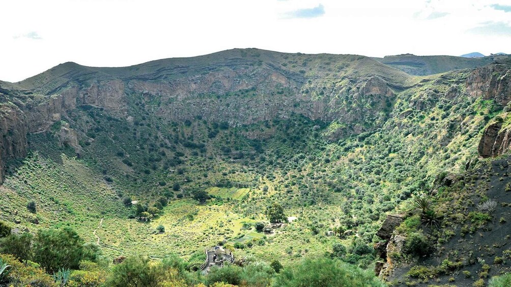 A mountainous landscape with a valley, dense vegetation, and a small structure at the valley's base. 1