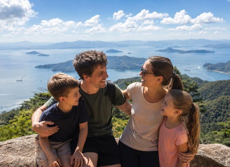 A family of four sitting on a rock overlooking a coastal landscape with mountains and islands in the distance. 1
