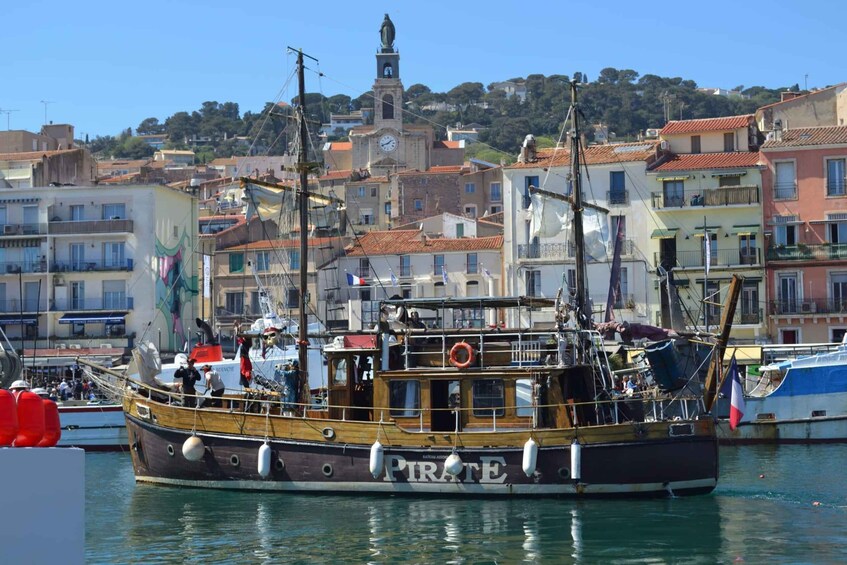 A large wooden boat named 'Pirate' docked in a harbor with colorful buildings and a church in the background. 2