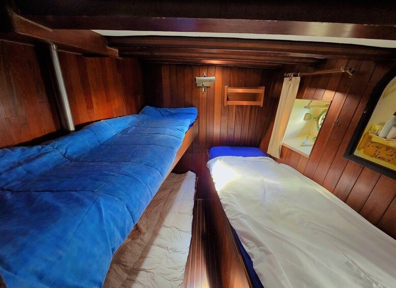 A narrow cabin with two beds, wooden walls, and a small window. 3