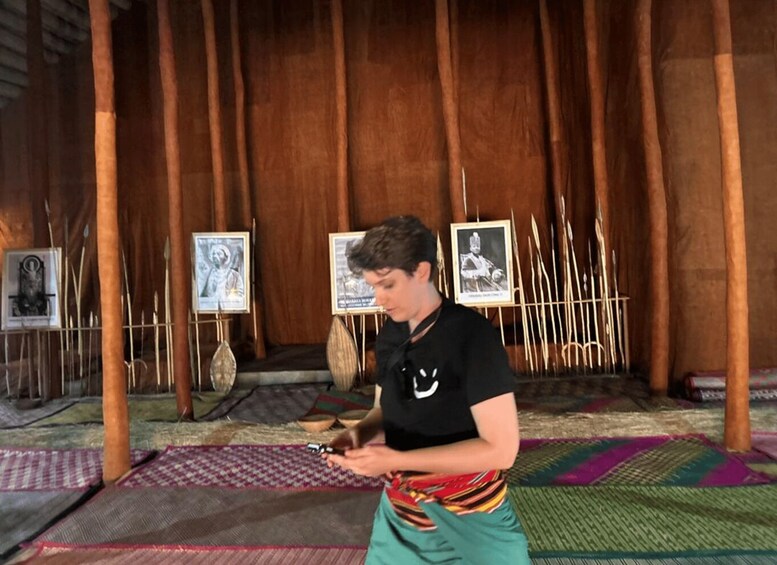 A person in traditional attire sitting on a mat, surrounded by wooden structures and framed pictures. 2