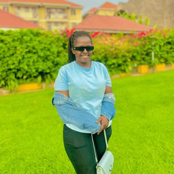 A person in a blue shirt and denim jacket standing in a grassy area with a white handbag. 3