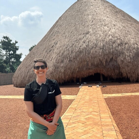 A person standing in front of a large thatched structure with a brick pathway leading to it. 5