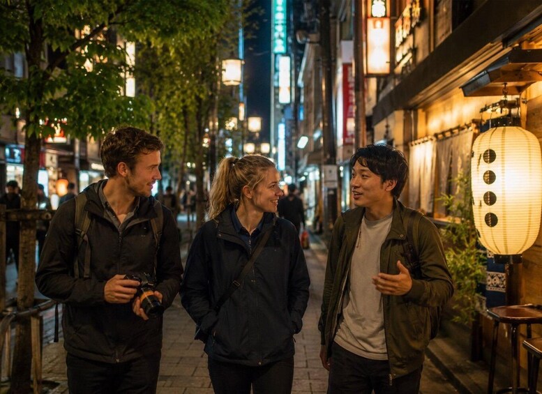 Three people walking on a city street at night with illuminated signs and a traditional lantern. 4