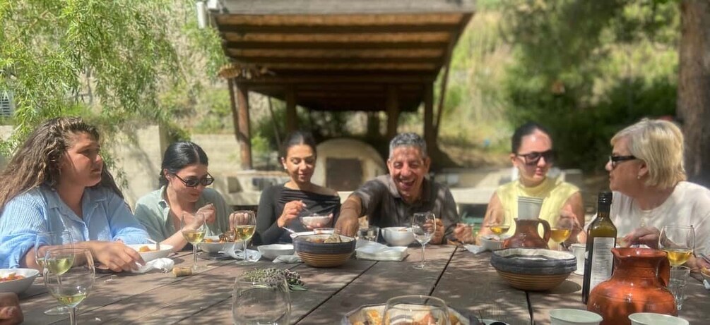 A group of people dining outdoors at a wooden table with wine glasses and bowls. 4