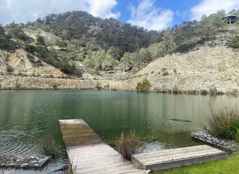 A calm lake with a wooden dock extending into the water, surrounded by hills with sparse vegetation. 1