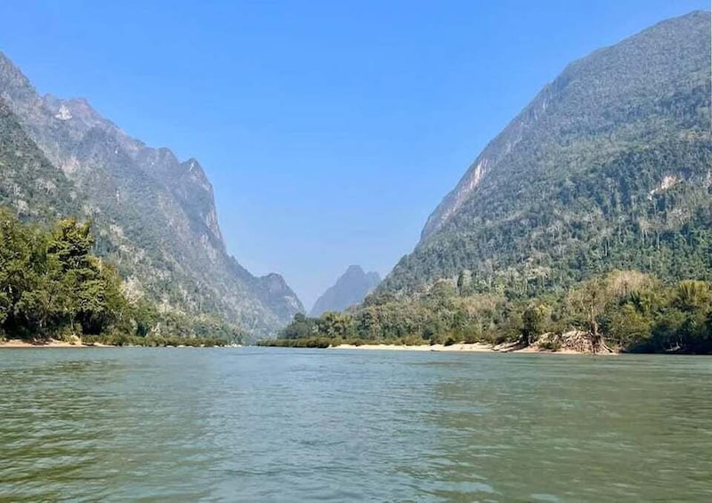 A river flanked by steep, forested mountains under a clear sky. 2
