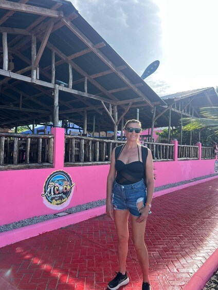 A person standing in front of a pink building with a logo that reads 'At Coco Restaurant.' 1