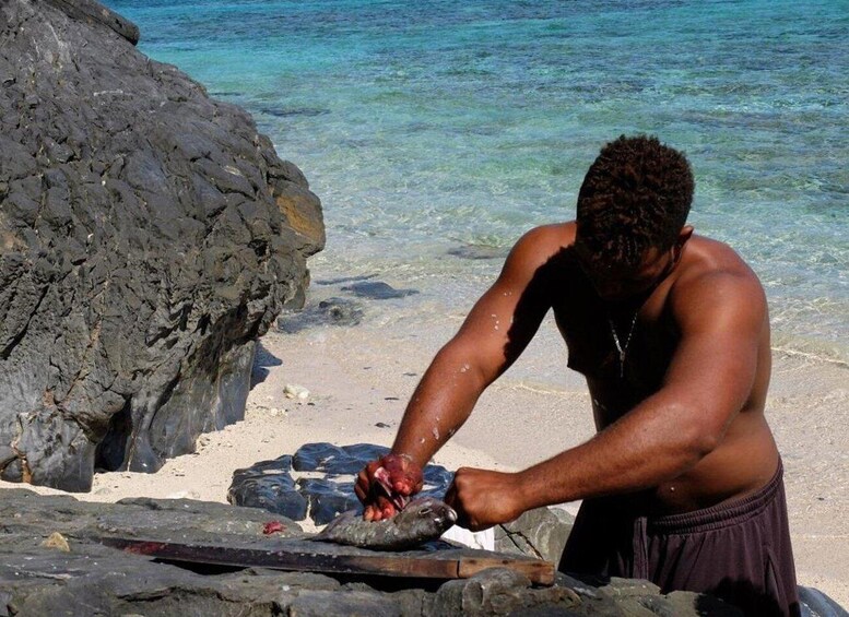 Una persona en la playa, con agua cristalina, una roca grande y una parrilla. 3