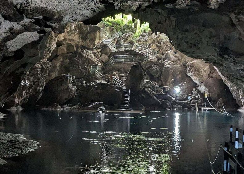 A cave with a water pool, rocky walls, and a metal staircase leading to a higher level. 3