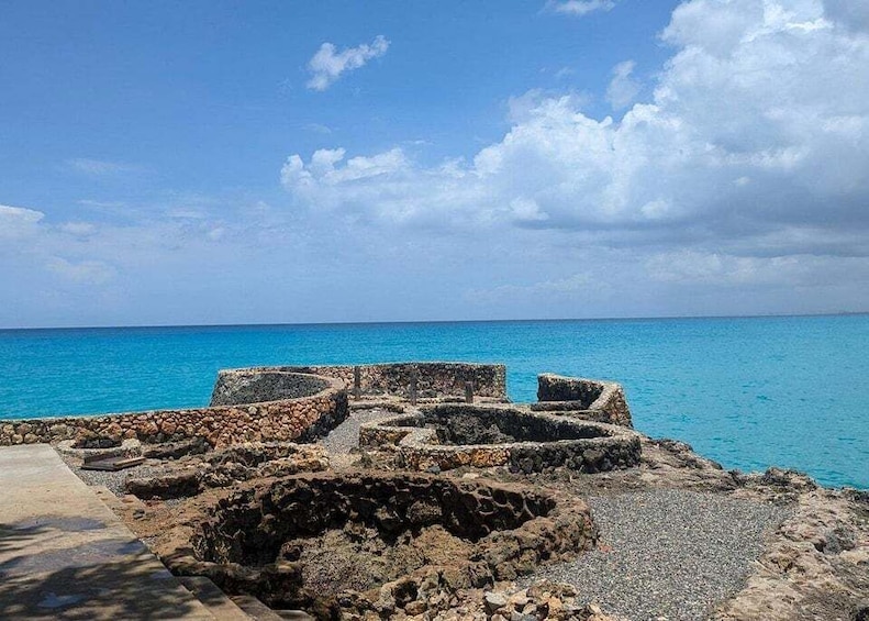 Ancient stone ruins by a turquoise sea under a partly cloudy sky. 1