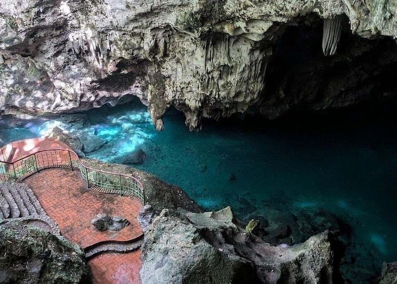 A cave with a red brick pathway leading to a pool of clear blue water. 2
