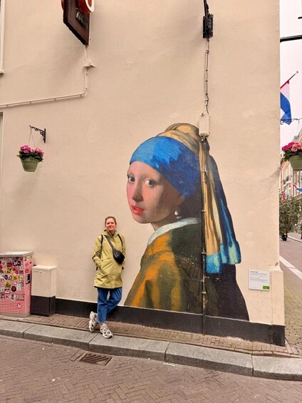 A person standing next to a large mural of a woman with a blue and yellow headscarf. 3