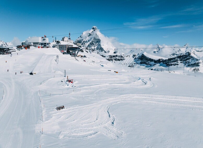 A snow-covered ski slope with a chairlift, buildings, and a mountain peak. 3