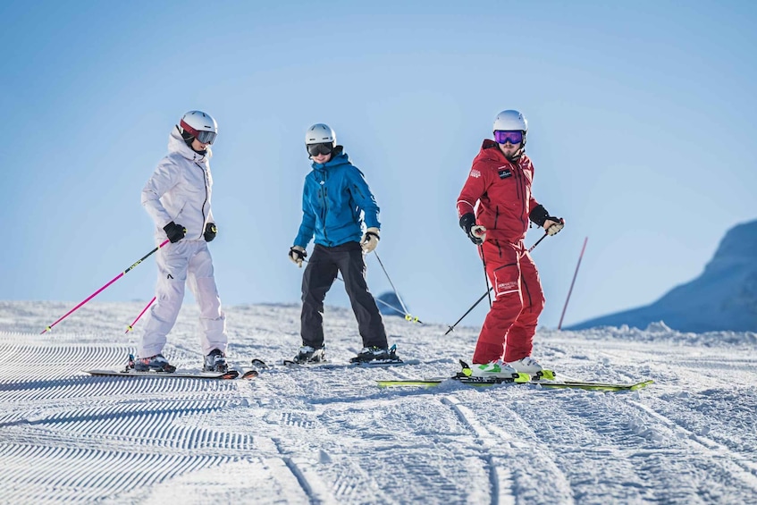 Three skiers on a snowy slope with skis and poles, wearing helmets and goggles. 1