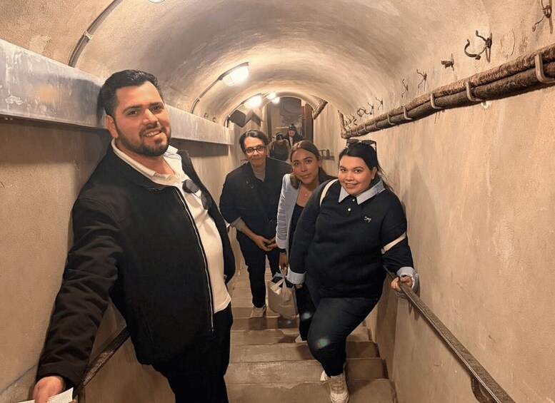 A group of people descending a stone staircase in a tunnel with metal railings and decorative elements. 1