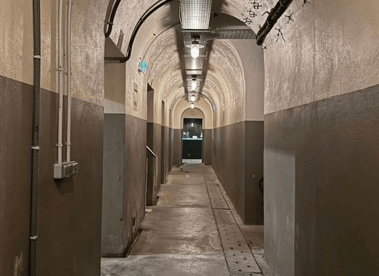 A long, arched hallway with concrete walls and a metal ceiling, leading to a door at the end. 2