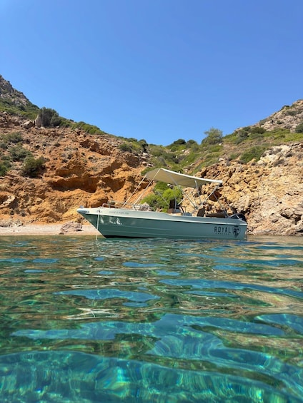 A boat named 'ROYAL RC' anchored in clear water with a rocky hillside in the background. 3