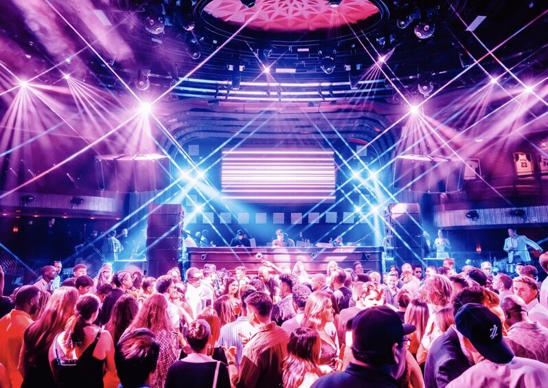 A crowded indoor venue with a stage, bright lights, and a large audience. 3