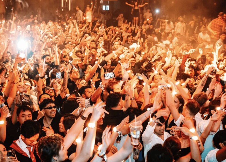 A crowded event with people holding up phones and light sticks. 4