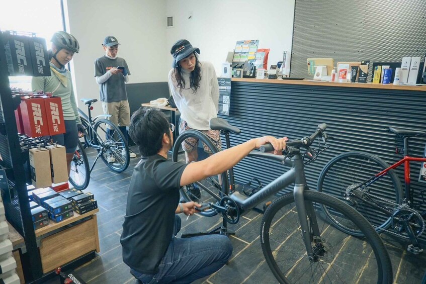 A bicycle repair shop with a man fixing a bike, a woman in a white hoodie, and another person using a phone. 5