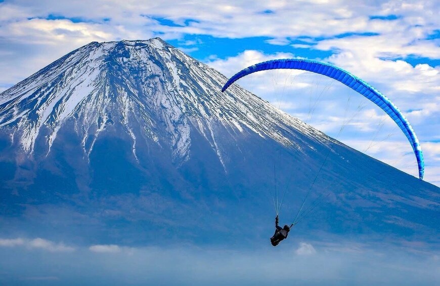A person paragliding near a snow-capped mountain. 1
