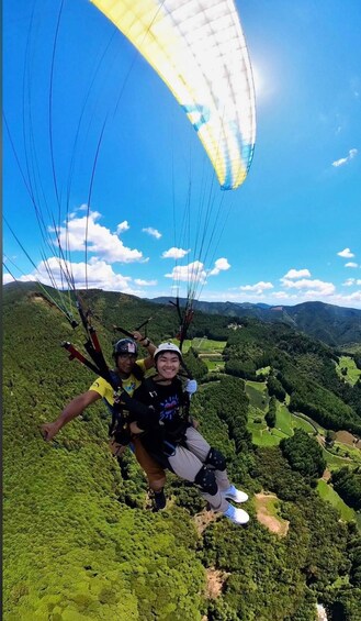 Two people paragliding over a lush green valley with mountains in the background. 2
