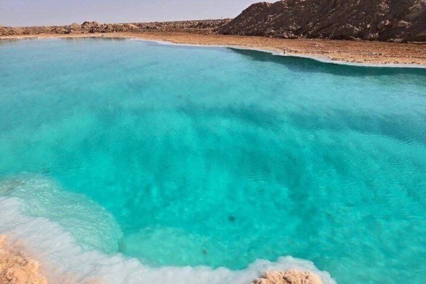 A turquoise pool with clear water, surrounded by rocky terrain. 1