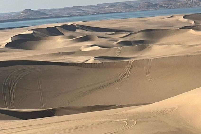 Undulating sand dunes with a body of water in the background. 3