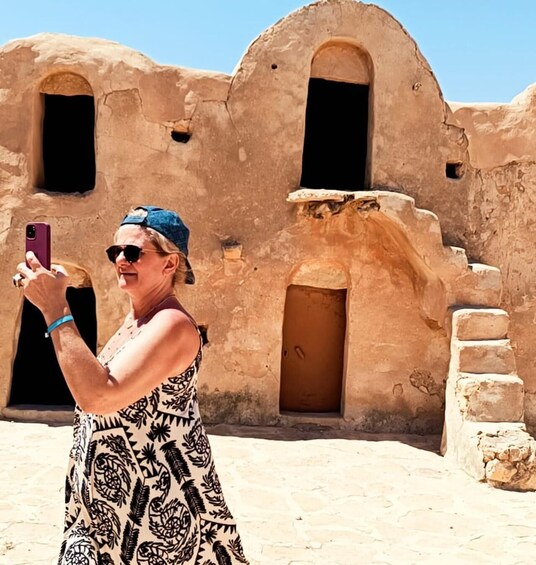 A person taking a photo with a smartphone in front of a historic building with arched doorways. 1