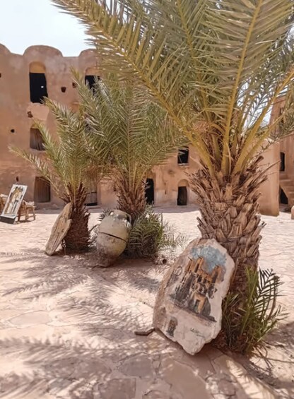 A courtyard with palm trees, a mural, and a building with arched windows. 4