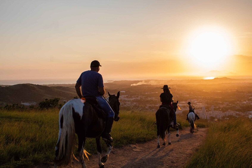 A sunset over a hilly landscape with people horseback riding. 1
