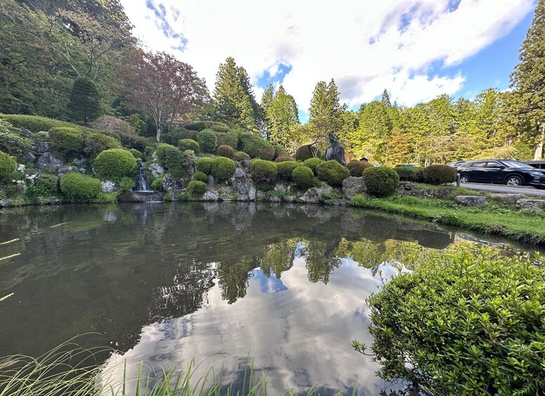 A tranquil pond surrounded by lush greenery and trees, with a clear reflection of the sky and clouds. 2
