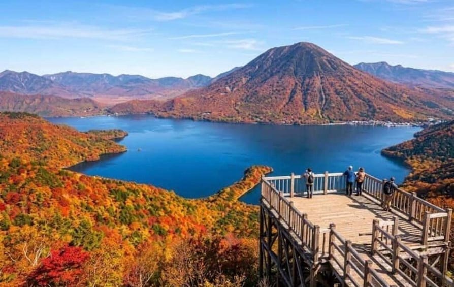 A lake surrounded by autumn-colored hills, a wooden viewing platform, and distant mountains. 4