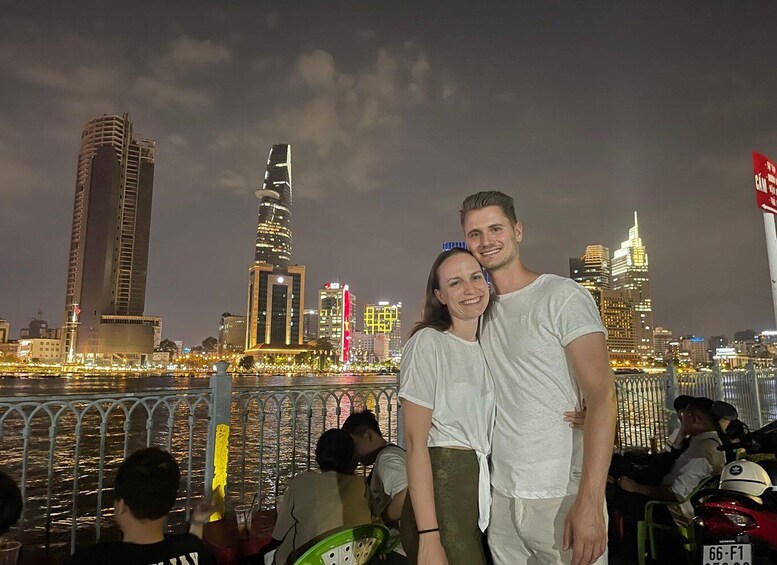 A couple standing on a bridge with a city skyline in the background. 1