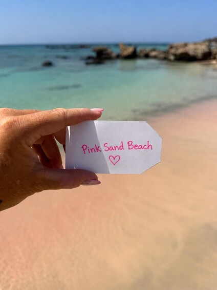 A hand holding a paper with 'Pink Sand Beach' written on it. 1