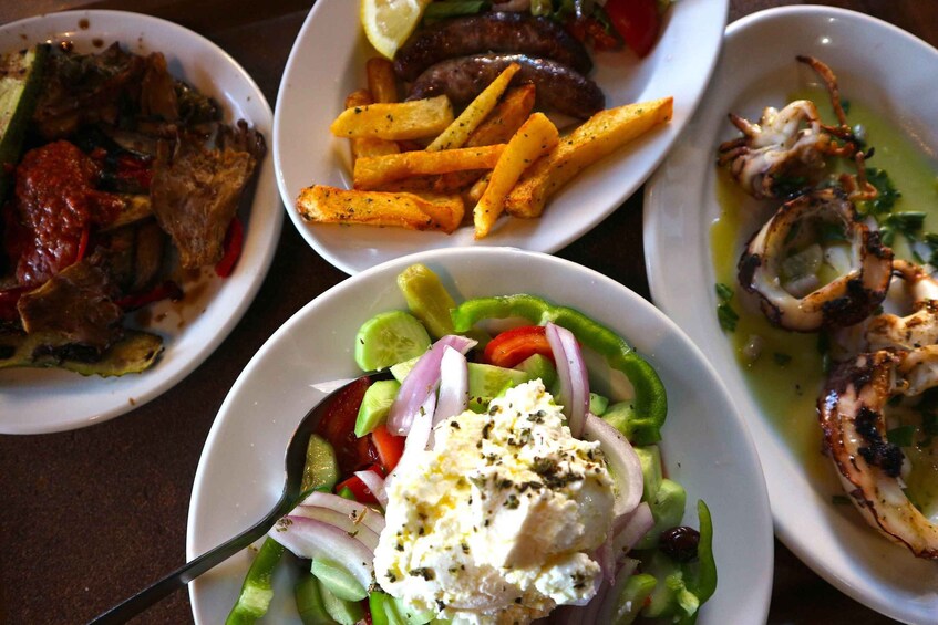 A variety of dishes including a salad with feta cheese, grilled octopus, and a plate of sausages. 3
