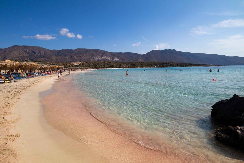 A beach with clear turquoise water, a sandy shore, and mountains in the background. 1