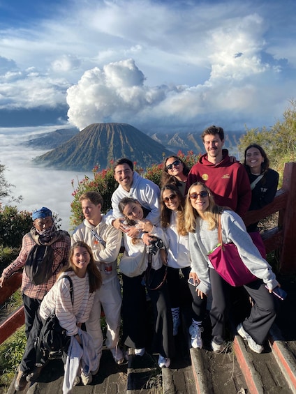 A group of people posing on a wooden platform with a mountain and clouds in the background. 3