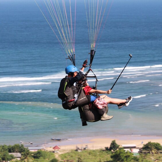 A person paragliding over a coastal area with the ocean and beach in the background. 1