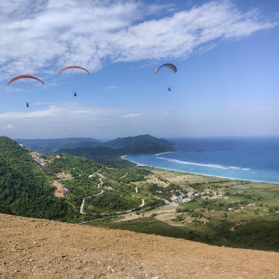 Paragliders flying over a coastal landscape with mountains and a winding road. 3